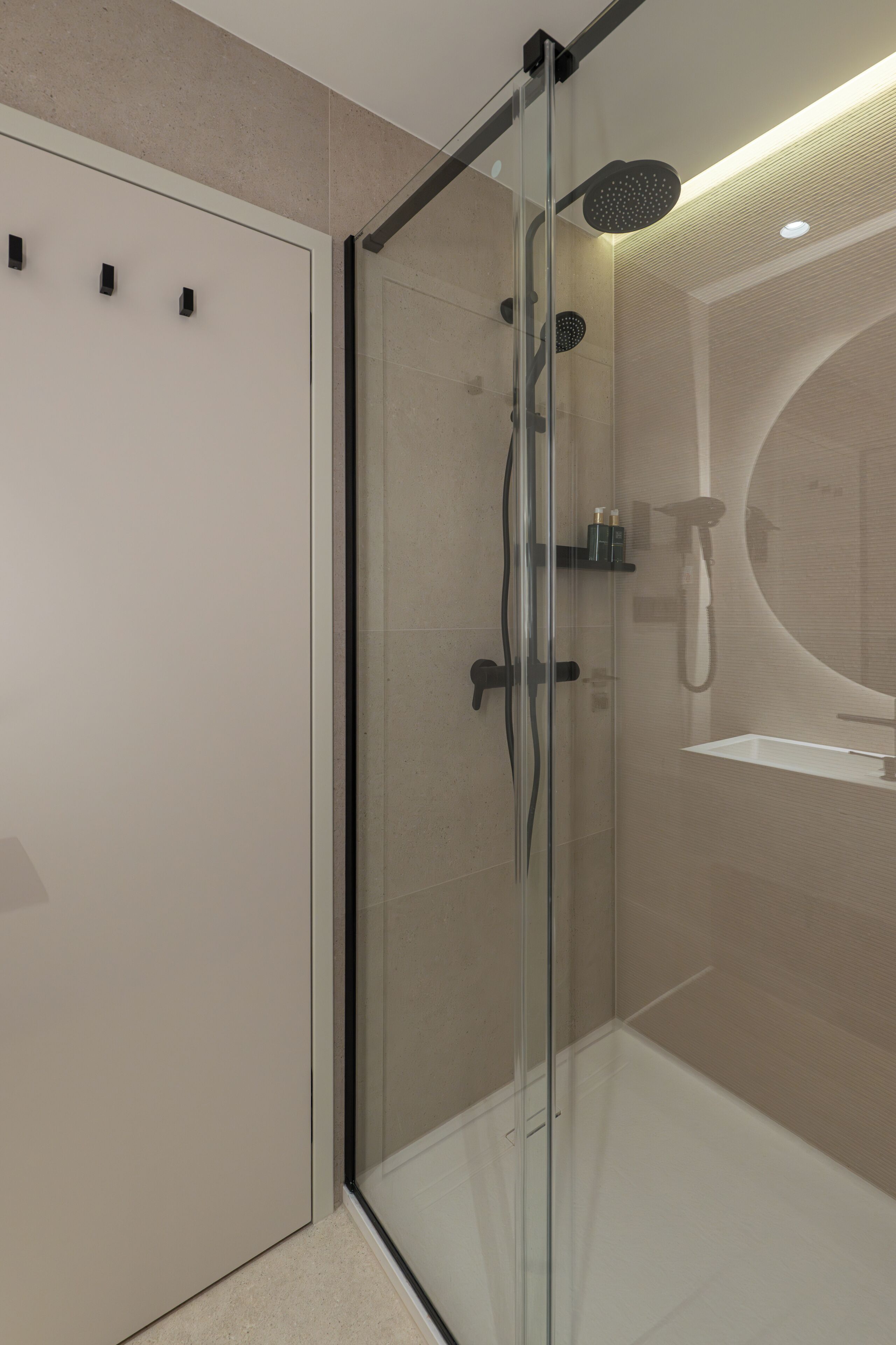 Un baño moderno con ducha de vidrio, un espejo redondo y un lavabo blanco.