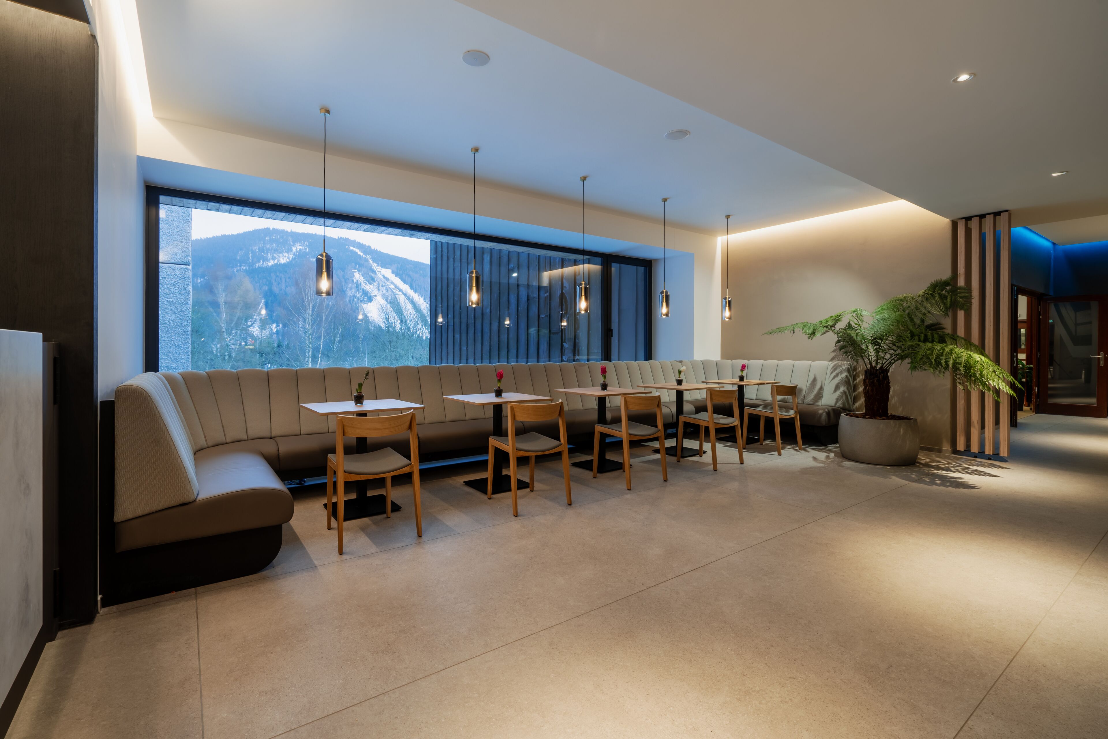 A modern interior with a sofa and tables, large windows, and a view of mountains.