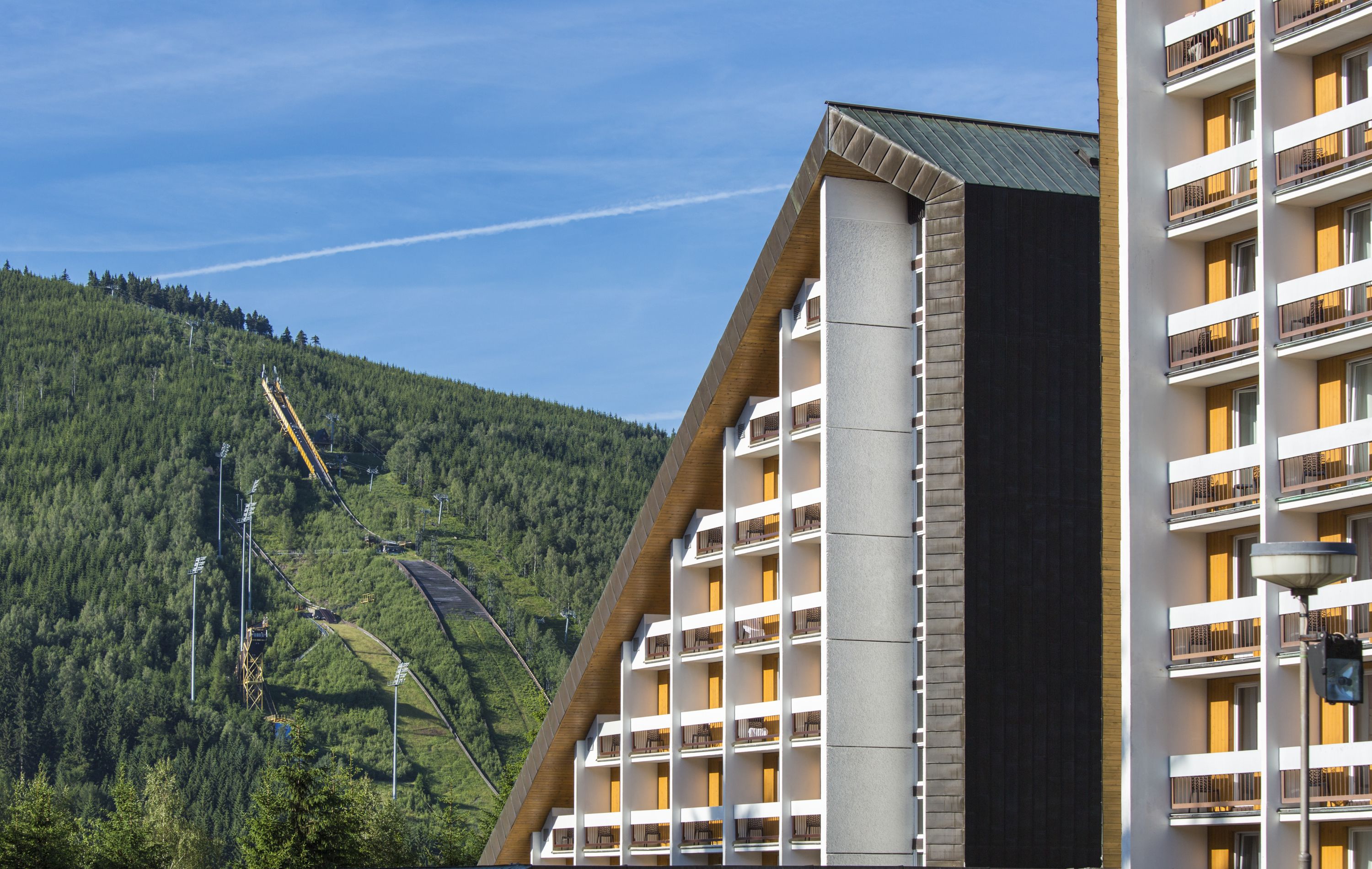 A modern hotel with multiple balconies, a ski lift in the background, and a mountainous landscape.