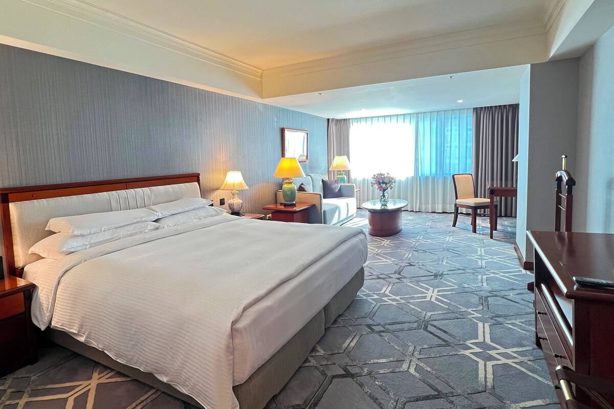 Une chambre d’hôtel avec un grand lit, deux tables de chevet avec des lampes, un canapé, un fauteuil et un bureau.
