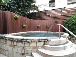 Egy jakuzzi, melyhez kőből készült lépcső vezet, és amelyet egy fa kerítés vesz körül, melyre virágcserepekben ültetett növények vannak kihelyezve.