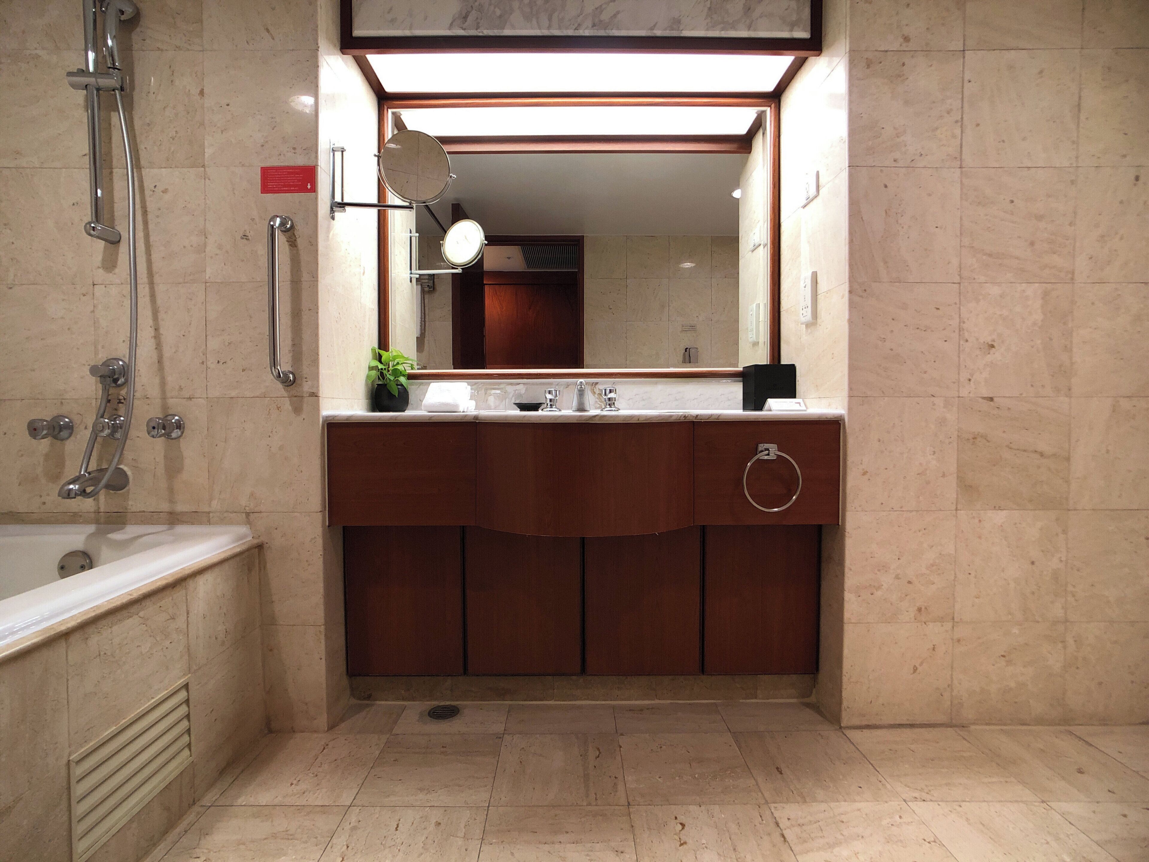 Un baño con bañera, ducha, lavamanos con espejo y una planta en maceta.