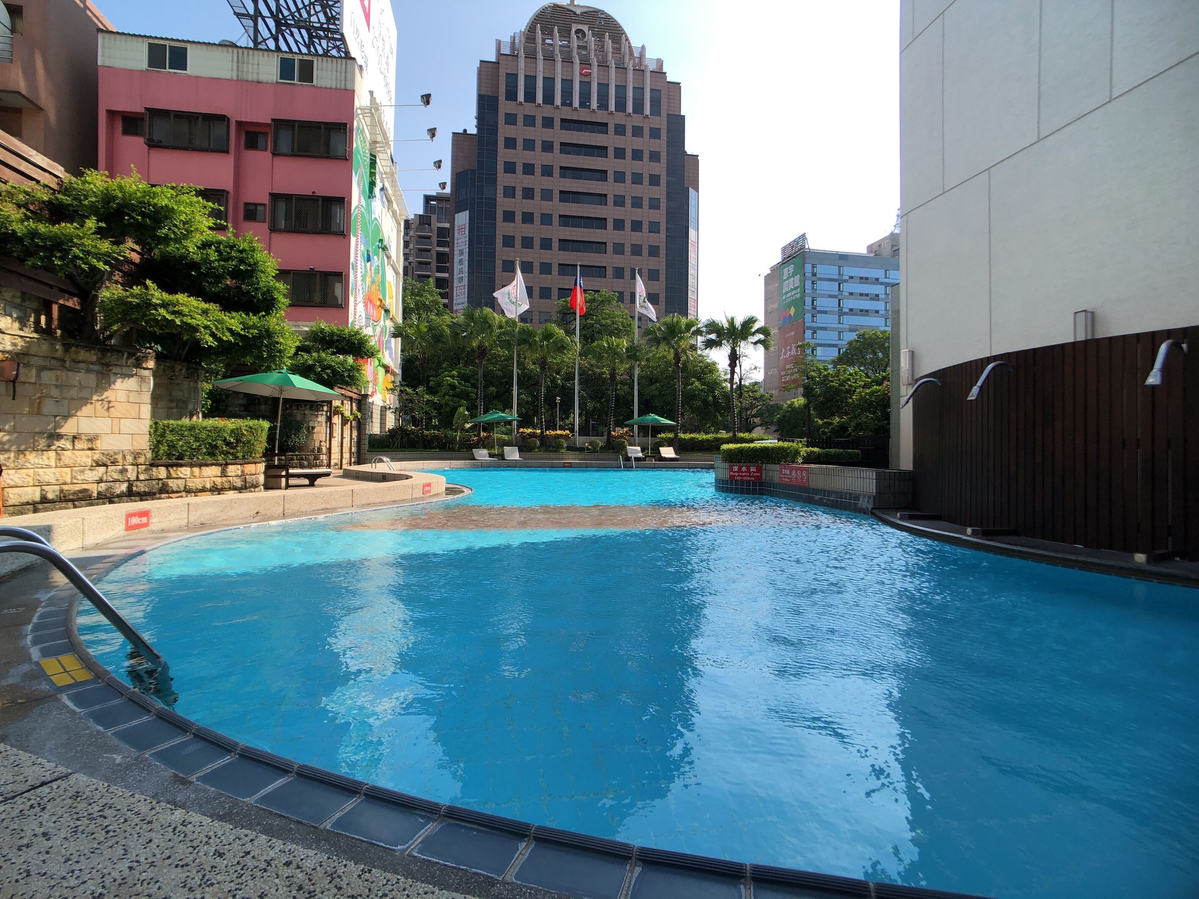 A swimming pool with a clear blue water, surrounded by buildings and greenery.