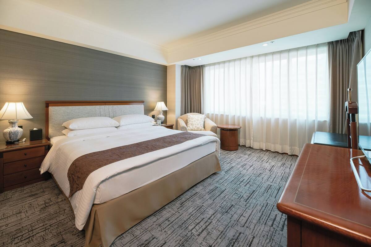Une chambre d’hôtel avec un grand lit, deux tables de chevet avec des lampes, une chaise, une petite table ronde et un téléviseur.