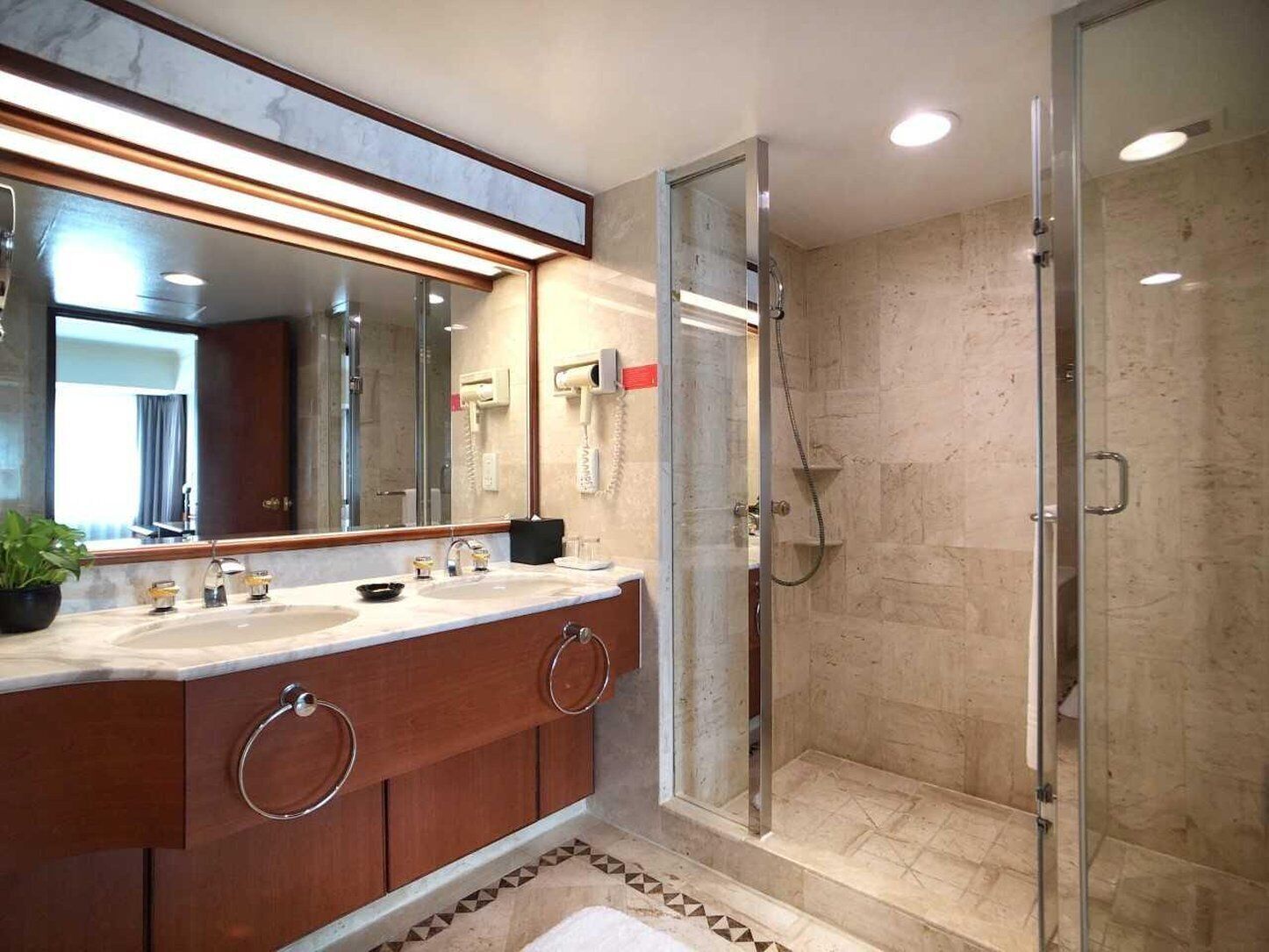 Un baño moderno con un espejo grande, dos lavamanos, cabina de ducha de vidrio y suelo de baldosas de mármol.