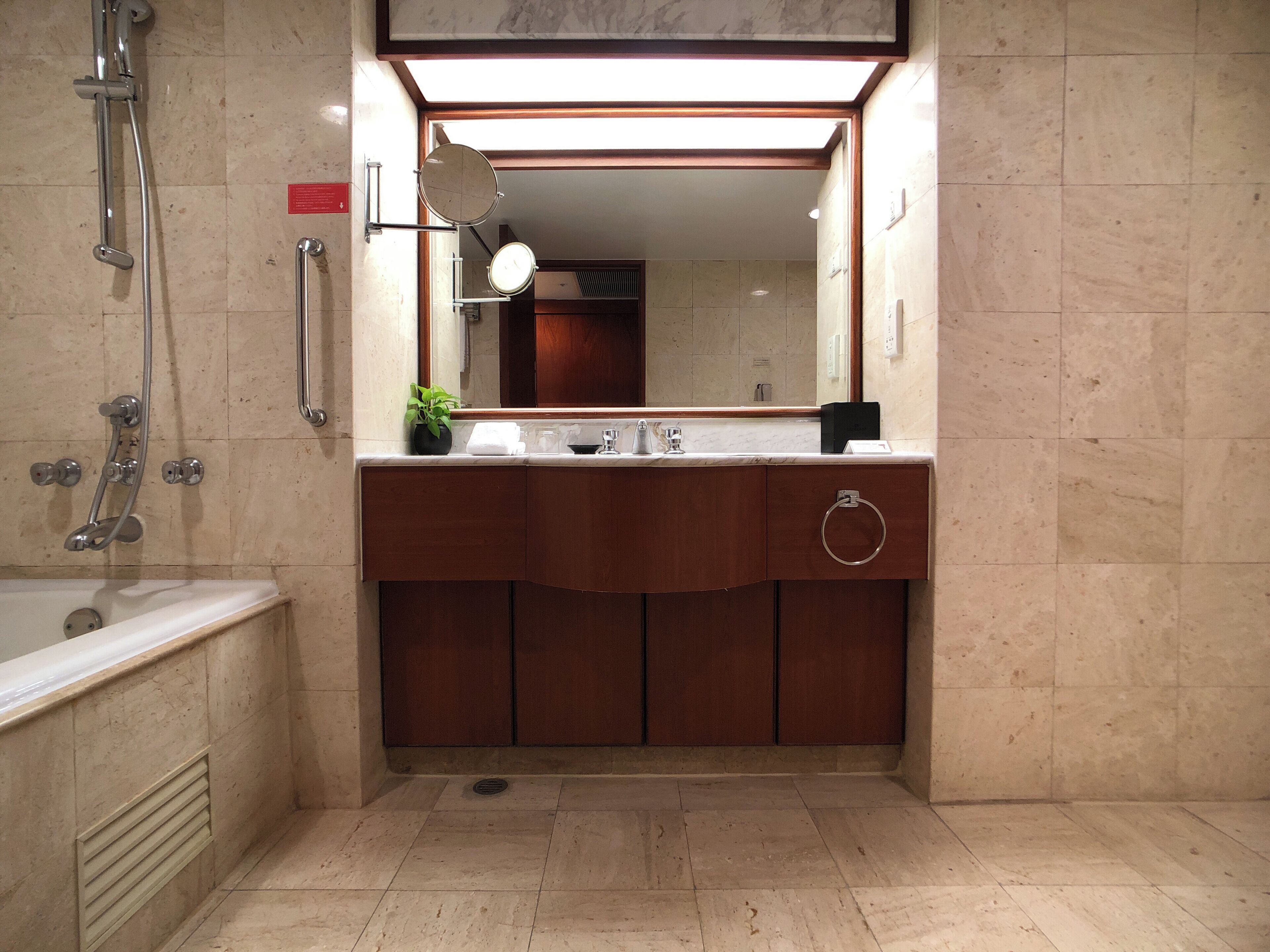 Un baño con bañera, ducha, lavamanos con espejo y una planta en maceta.