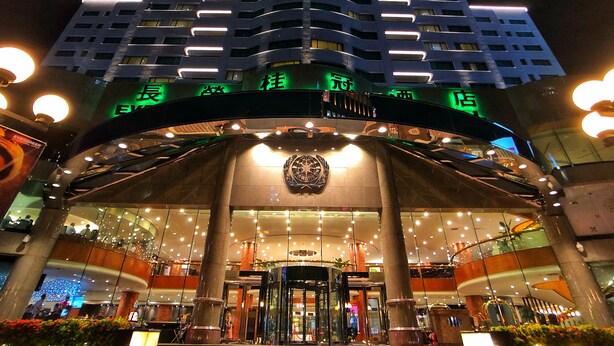 Een hotelgevel met modern ontwerp, met een grote glazen gevel en een opvallende ingang met een decoratieve wereldbol.
