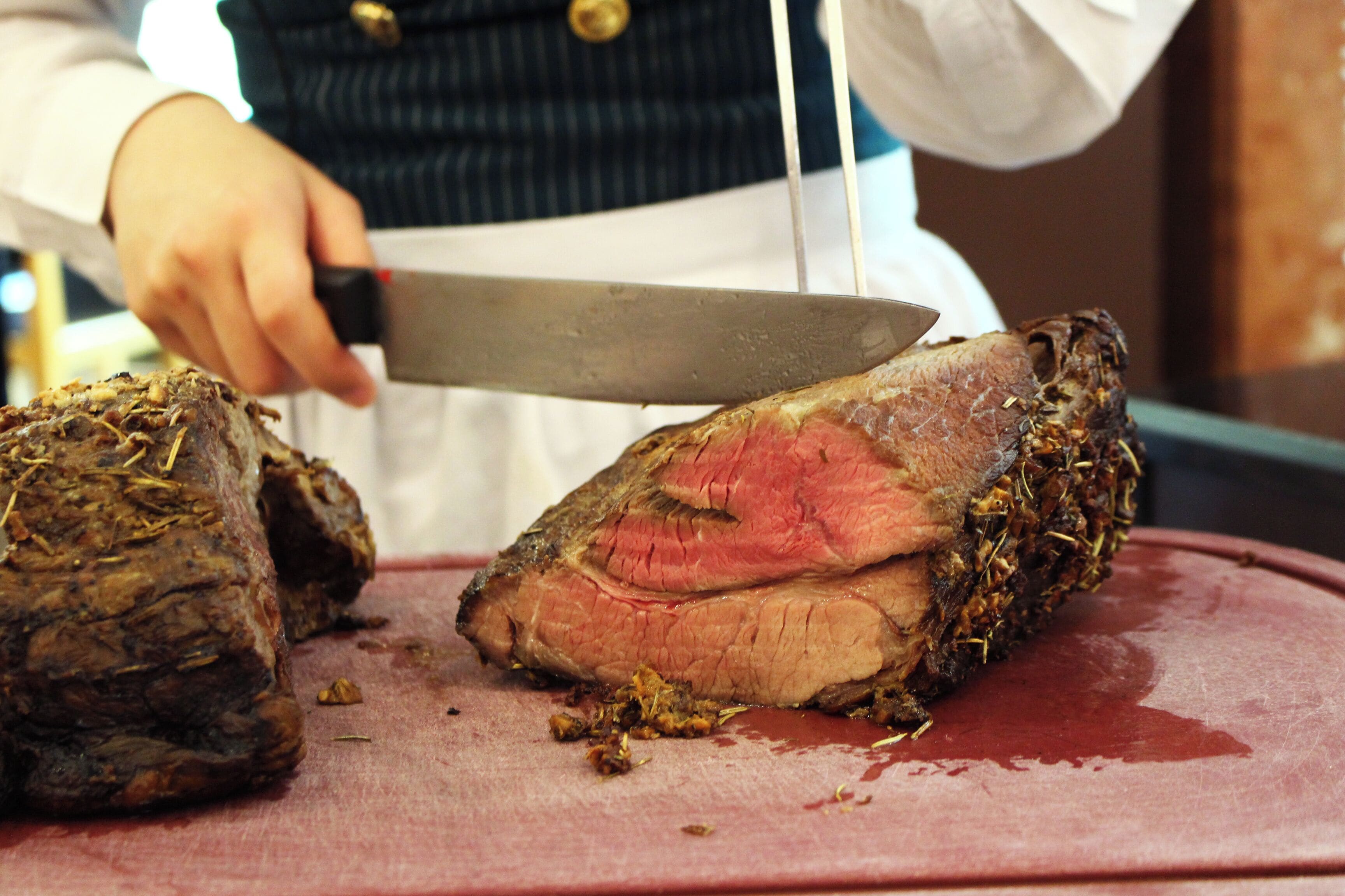A person slicing a large piece of meat on a cutting board.
