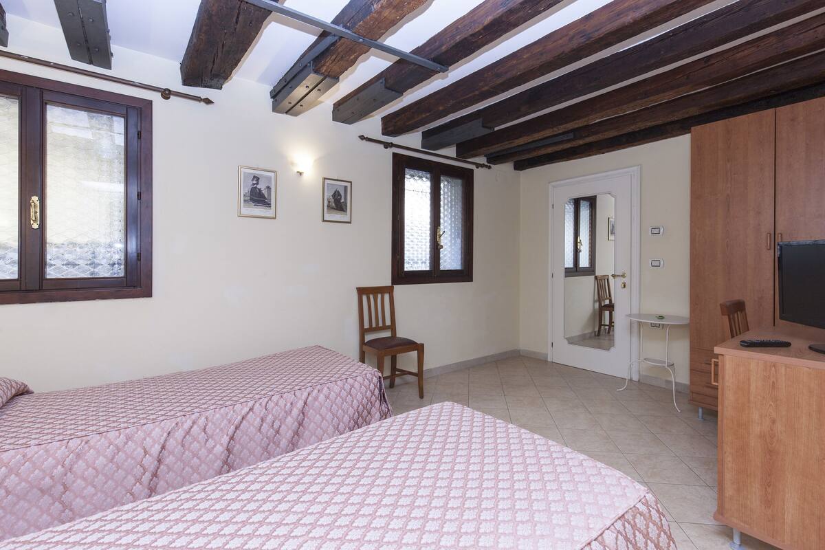 A bedroom with two beds, a wooden desk, a chair, and a television.