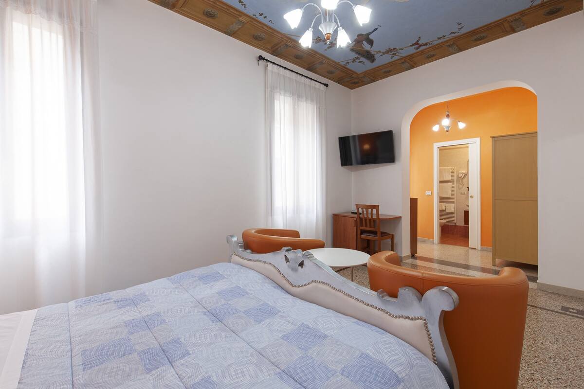 A hotel room with a bed, a small table, two chairs, a TV, and a bathroom visible through an archway.