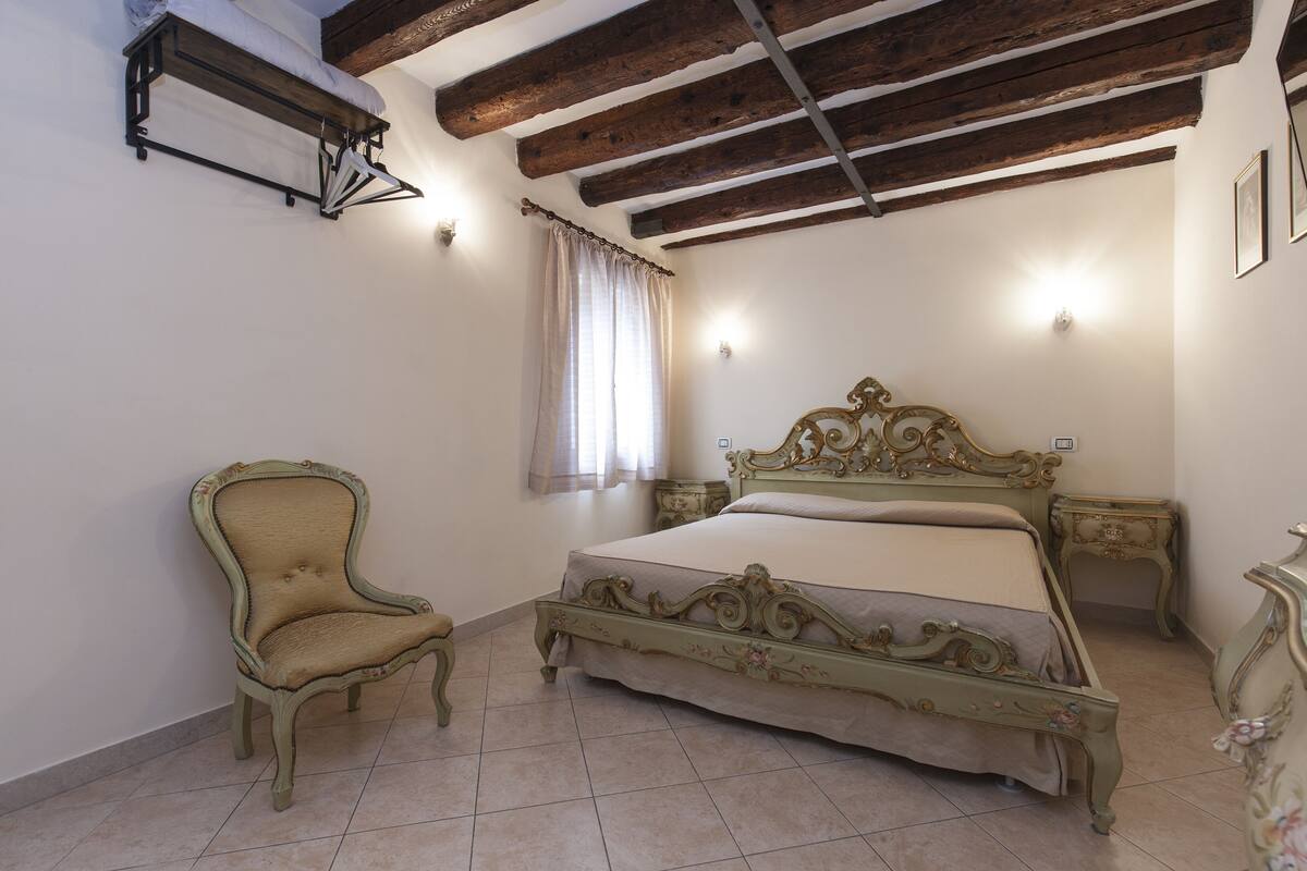 A bedroom with a large bed, a chair, a nightstand, and a wooden ceiling.