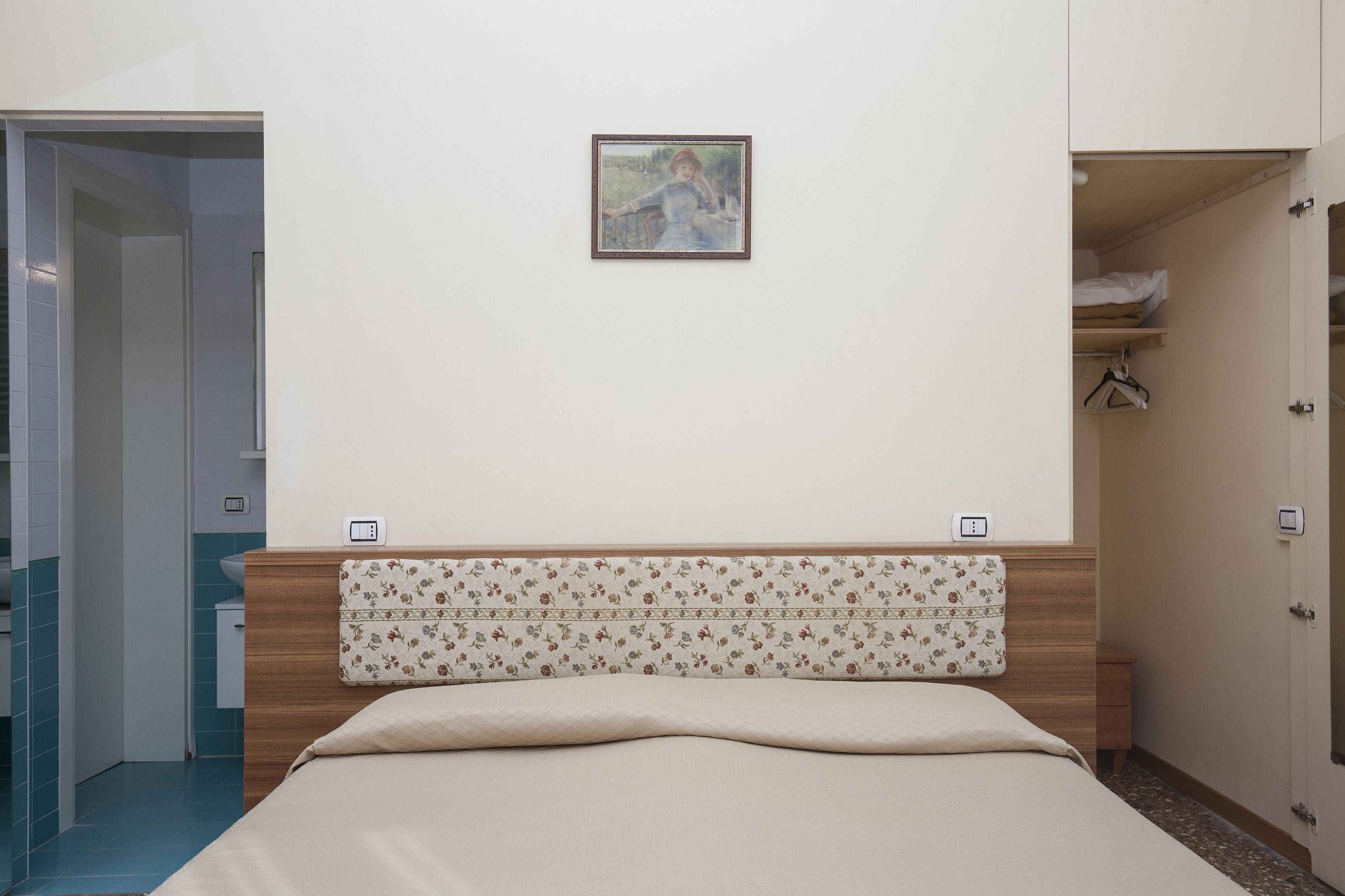 Une chambre à coucher avec un lit, une tête de lit à motifs floraux, un tableau au mur et une armoire avec un miroir.
