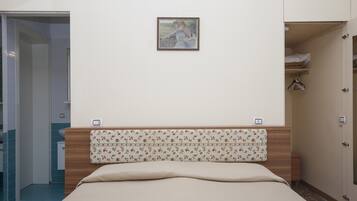 Une chambre à coucher avec un lit, une tête de lit à motifs floraux, un tableau au mur et une armoire avec un miroir.