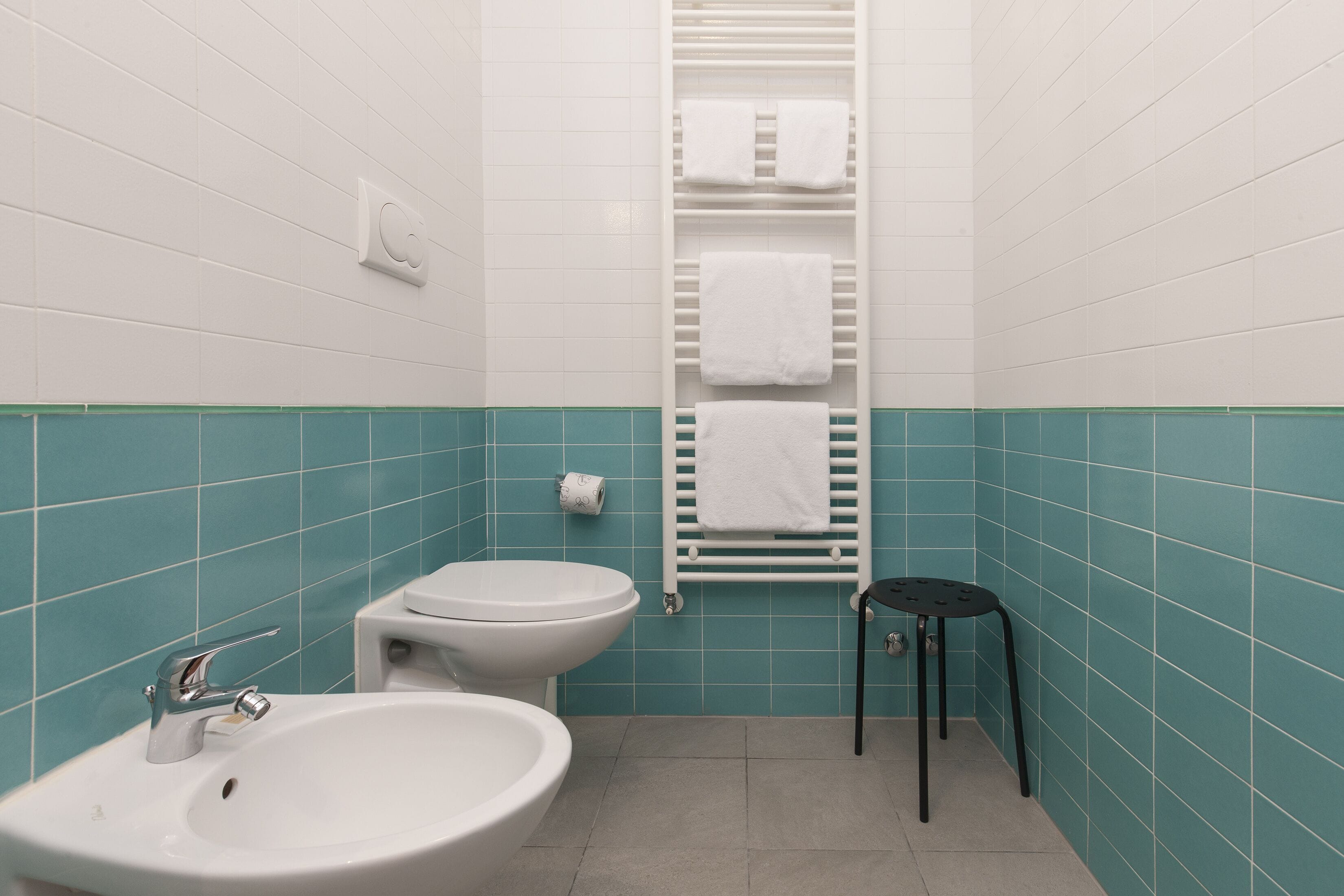 Une salle de bain équipée d’un lavabo, de toilettes, d’un porte-serviettes et d’un petit tabouret.