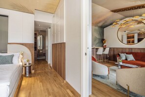 A modern hotel room with a wooden floor, a large bed, a sitting area with a red sofa, a round mirror, and a ceiling light fixture. - Hotel Val di Sogno (Malcesine)