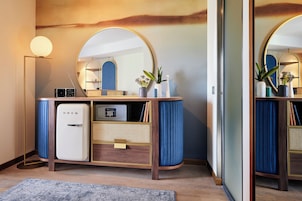A modern bathroom with a vanity, a mirror, a small refrigerator, and a floor lamp.
