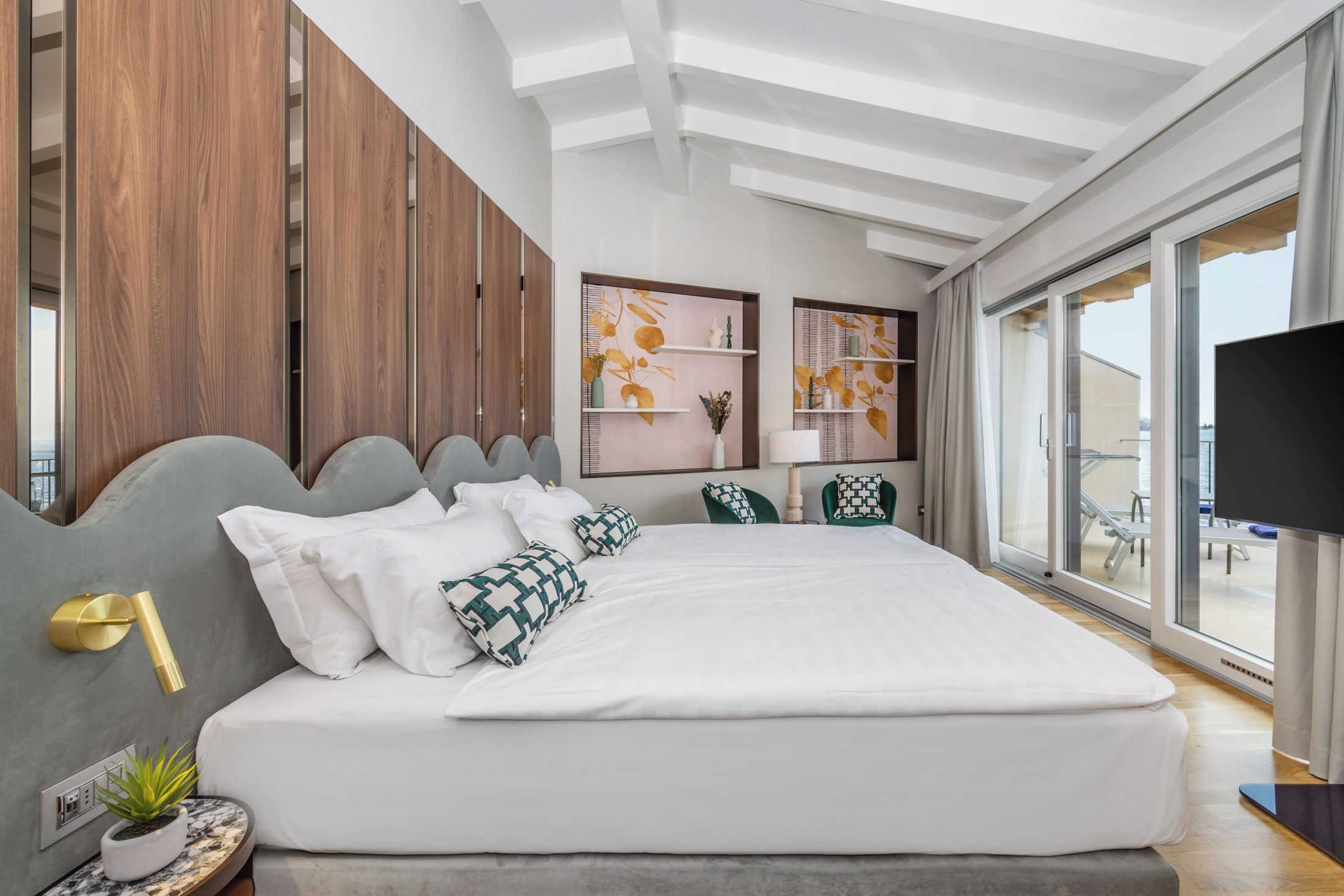 Un dormitorio moderno con una cama grande, paneles de madera, televisor y vistas al balcón.