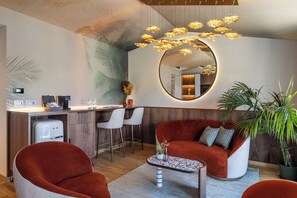 A modern living area with a sofa, chairs, a coffee table, a kitchen area, and a large mirror. - Hotel Val di Sogno (Malcesine)