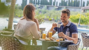 A couple dining outdoors with a view of a body of water and greenery. - Hotel Val di Sogno (Malcesine)