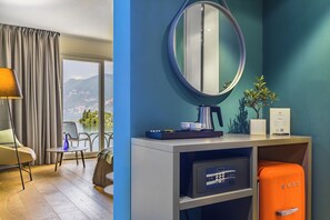 Una habitación de hotel moderna con vistas a montañas, un espejo redondo, un minibar y una maleta naranja.