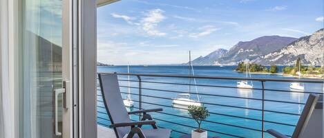 A balcony with two chairs and a small table, overlooking a marina with boats and a mountainous coastline.