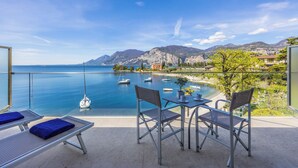 A balcony with a view of the sea, a table with chairs, and lounge chairs with towels. - Hotel Val di Sogno (Malcesine)