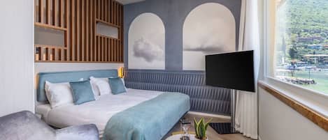 Un hotel moderno con una cama grande, televisión, una mesita con una planta y vistas a un paisaje montañoso a través de una ventana.