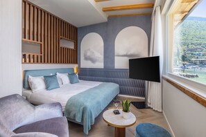 A modern hotel room with a large bed, a TV, a small table with a plant, and a view of a mountainous landscape through a window. - Hotel Val di Sogno (Malcesine)