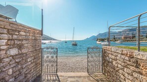 A stone pathway leading to a waterfront with boats and mountains in the background. - Hotel Val di Sogno (Malcesine)