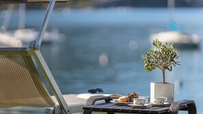 A table with a small potted plant, a plate with food, and a cup, set against a backdrop of a marina with boats. - Hotel Val di Sogno (Malcesine)