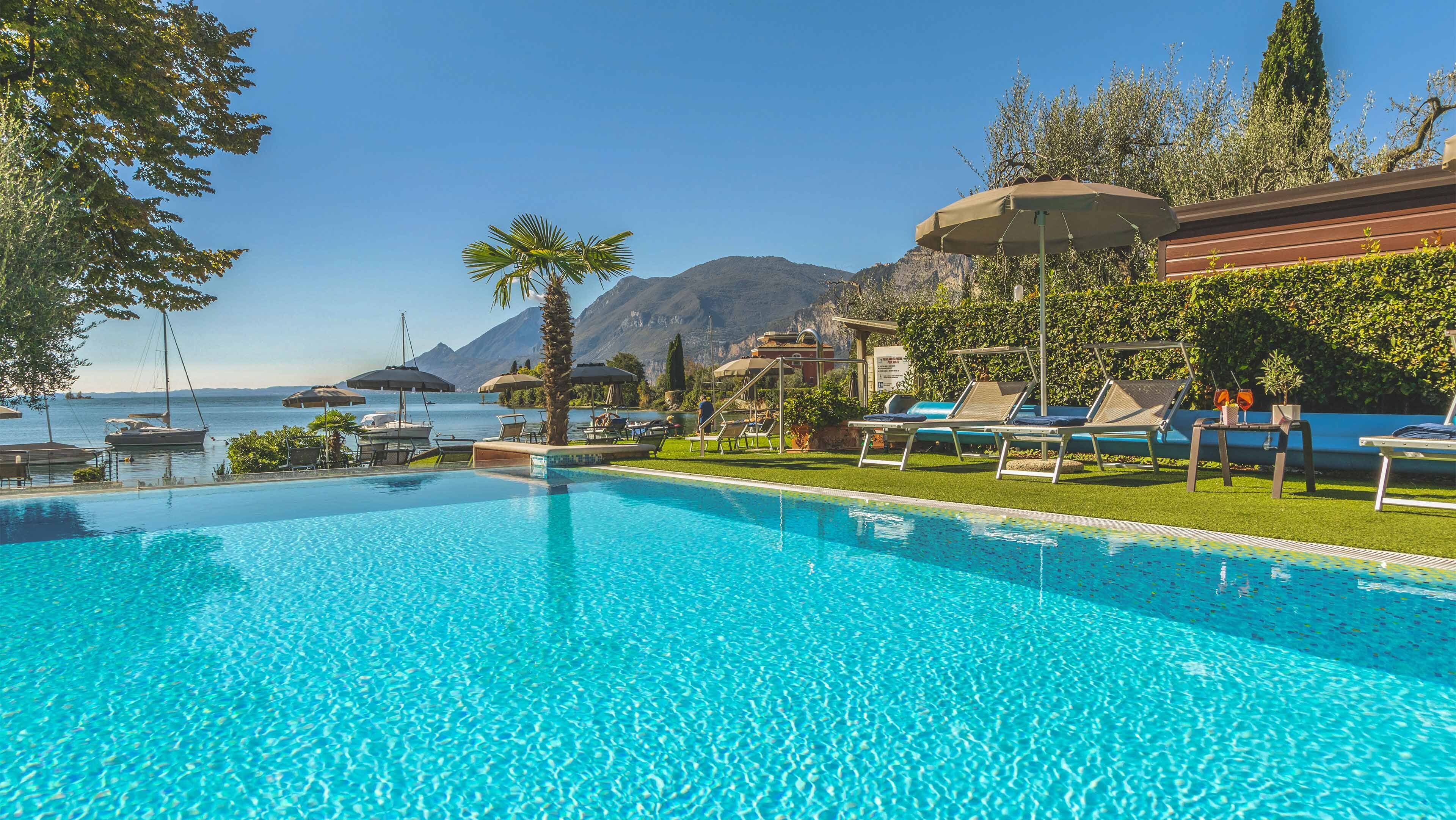 Une piscine d’un bleu éclatant, dotée de chaises longues et de parasols, avec une vue sur la mer et des montagnes en arrière-plan.