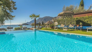 A clear blue pool with lounge chairs and umbrellas, a view of the sea, and mountains in the background.