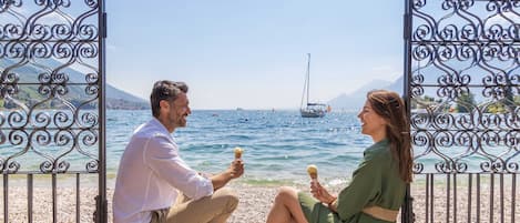Una pareja sentada en una playa de guijarros, con vista al mar y a los barcos.