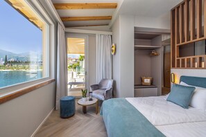Una habitació d'hotel amb un llit gran, una zona de seients amb una taula petita, una cadira i vista a una piscina i muntanyes.