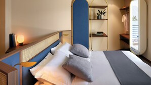A neatly made bed with pillows, a bedside lamp, a mirror, and a shelf with books and a plant. - Hotel Val di Sogno (Malcesine)