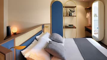 A neatly made bed with pillows, a bedside lamp, a mirror, and a shelf with books and a plant.