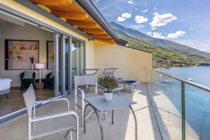 A balcony with a table and chairs, a potted plant, and a view of a lake and mountains. - Hotel Val di Sogno (Malcesine)