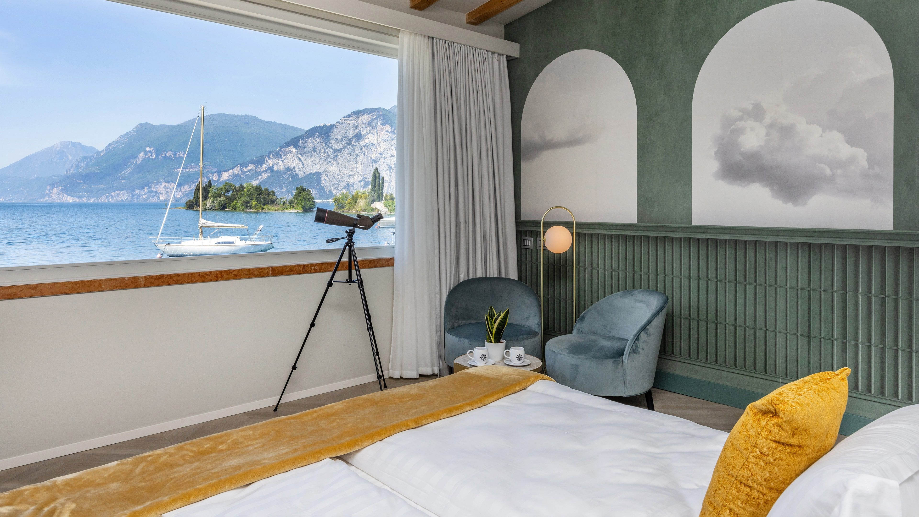 Une chambre à coucher avec un lit, un télescope, une chaise et une vue sur un lac où l’on peut voir des bateaux.