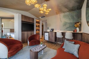 A modern living room with a TV, red sofas, a coffee table, and a kitchen area with bar stools. - Hotel Val di Sogno (Malcesine)