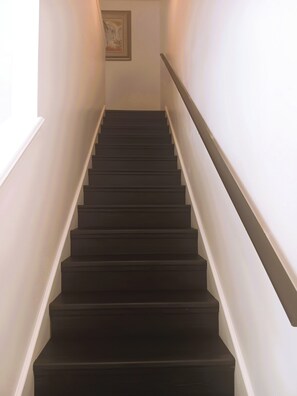 A staircase with dark steps and white walls, leading to a landing where a framed picture is visible. - The Cozy Inn (St. Augustine)