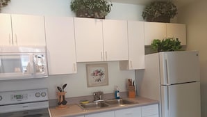 A kitchen with white cabinets, a microwave, an oven, a sink, and a refrigerator. - The Cozy Inn (St. Augustine)