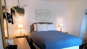 Ett välordnat hotellrum med en stor säng, två sänglampor, ett nattduksbord med en lampa, en hängande växt, en inramad tavla på väggen och en stol.