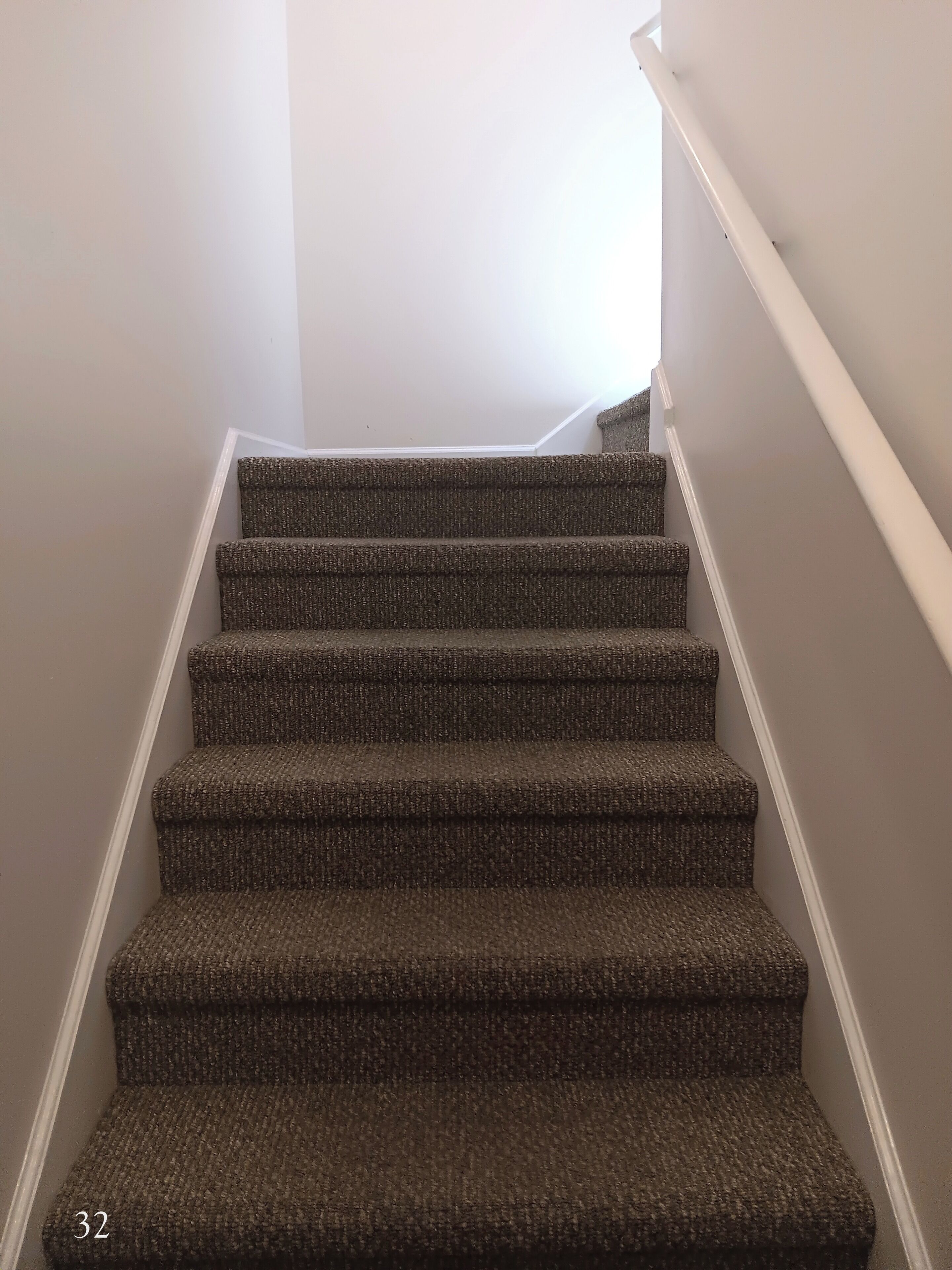 A carpeted staircase with white handrails and a plain wall.