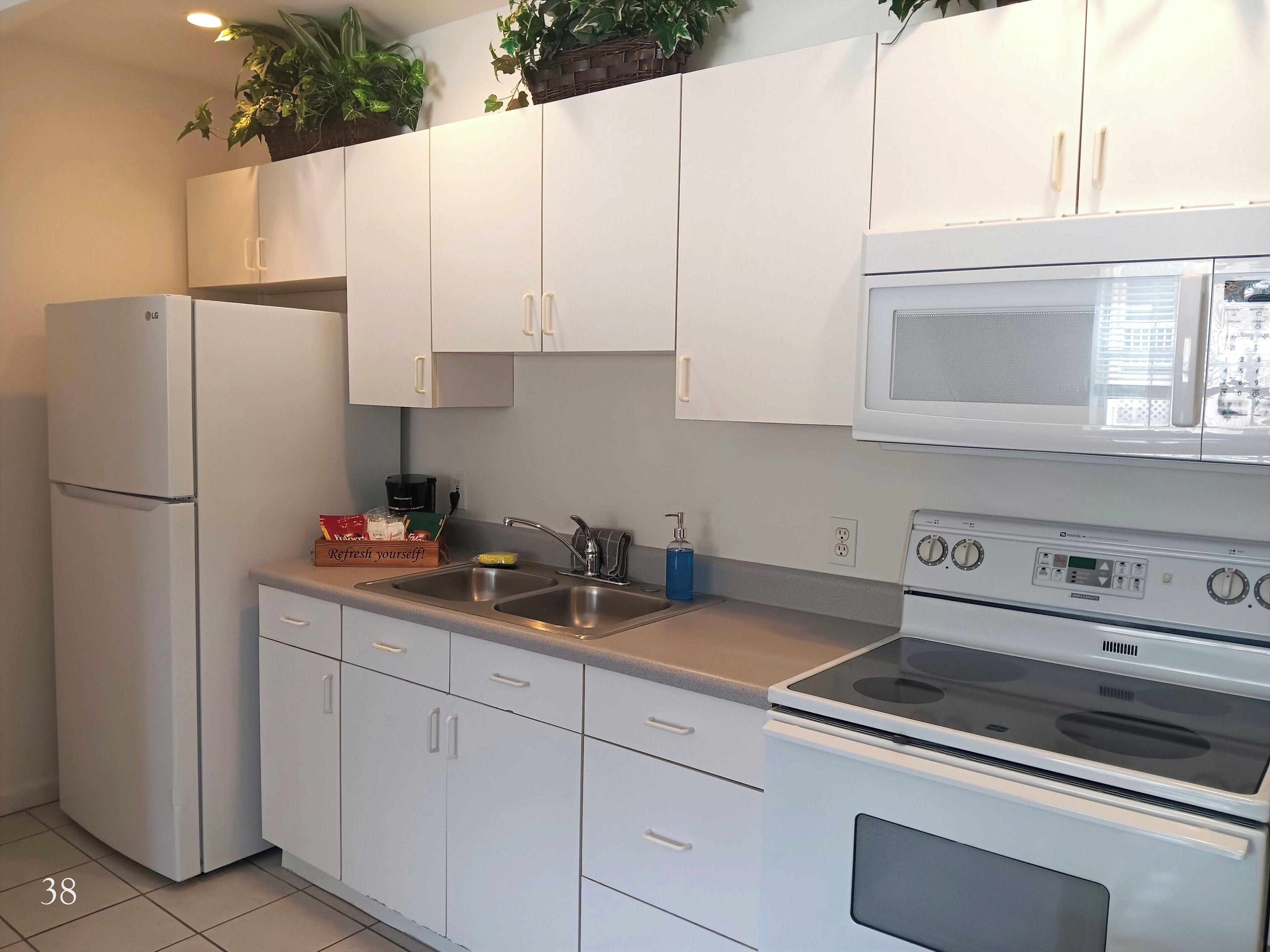 A compact kitchen with white cabinets, a built-in microwave, a stainless steel sink, and a stove.