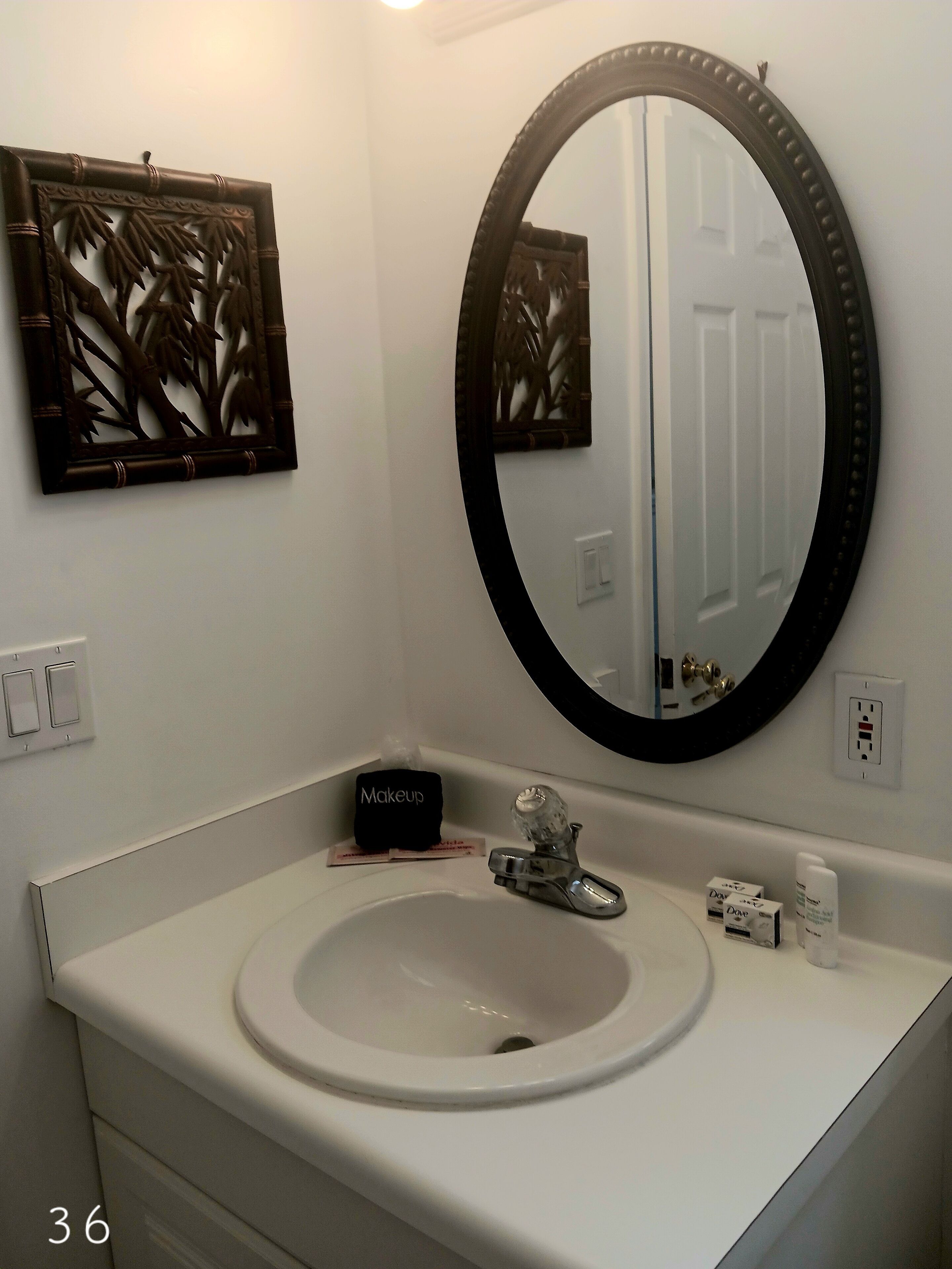 A bathroom with a white sink, a mirror with a black frame, and a decorative panel above the mirror.