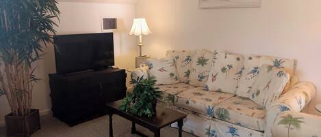 A living room with a sofa, a television, a lamp, and a potted plant.
