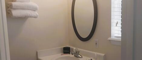 A small bathroom with a sink, mirror, and toilet. There are towels on a rack, a toilet paper holder, and a makeup mirror.