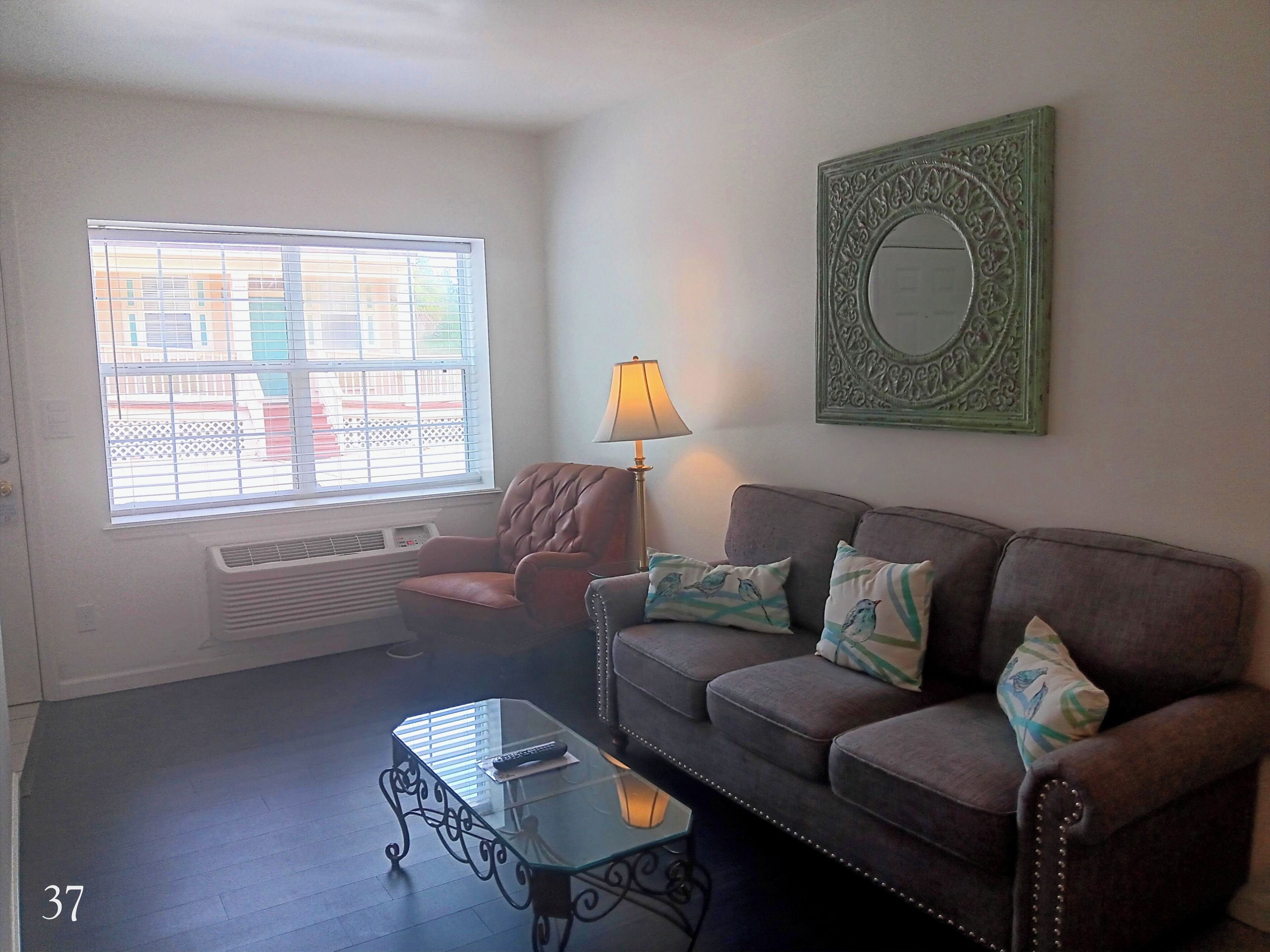 A living room with a leather couch, a glass coffee table, a lamp, and a window with blinds.