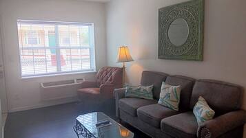 A living room with a leather couch, a glass coffee table, a lamp, and a window with blinds.