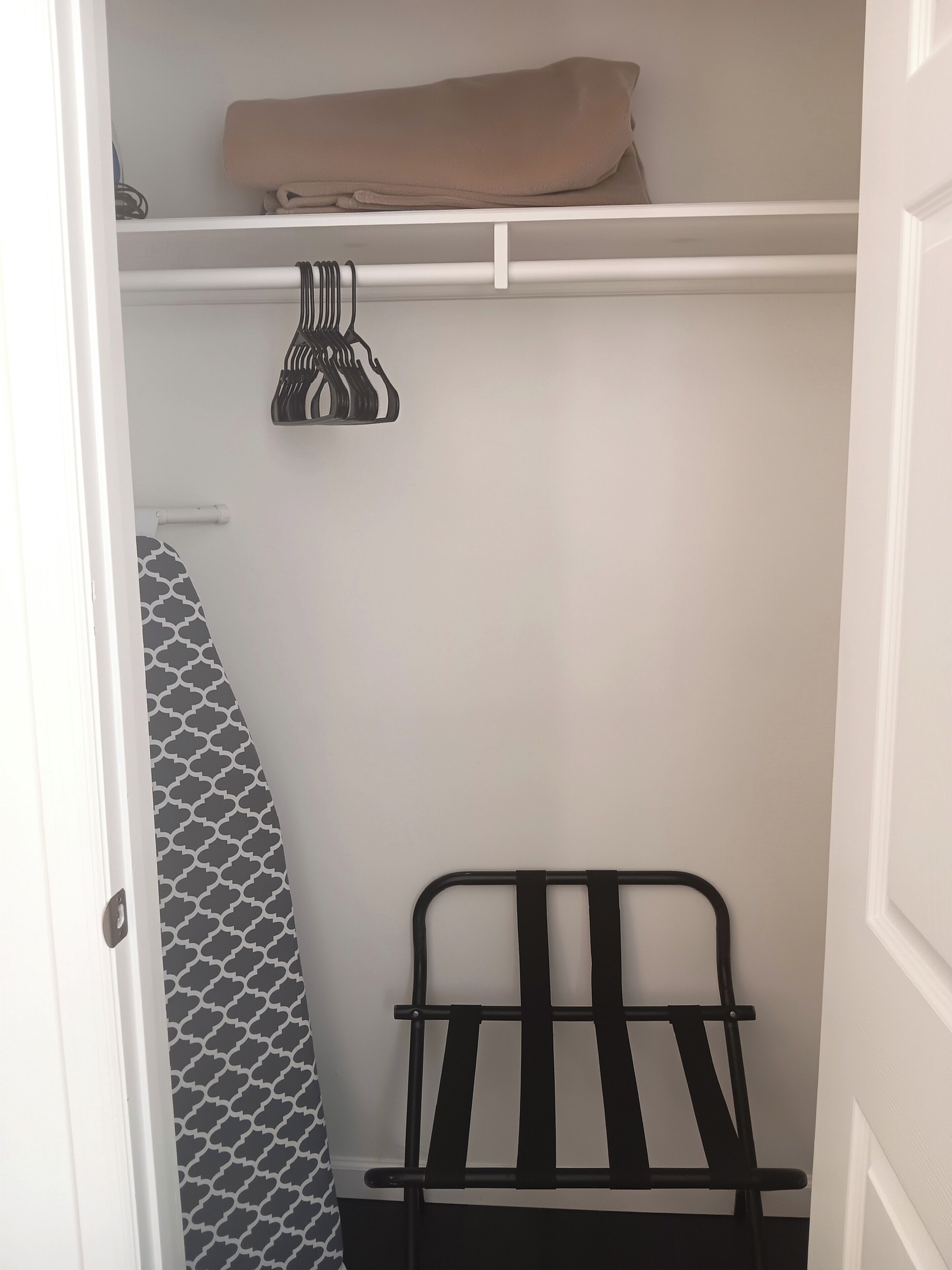 Ein begehbarer Kleiderschrank mit Kleiderstange, einer gefalteten Decke und einem gemusterten Duschvorhang.